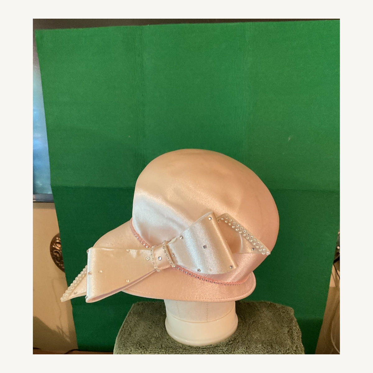 Blush satin-look cloche-style occasion hat with oversized bow and small crystal accents, pre-owned.