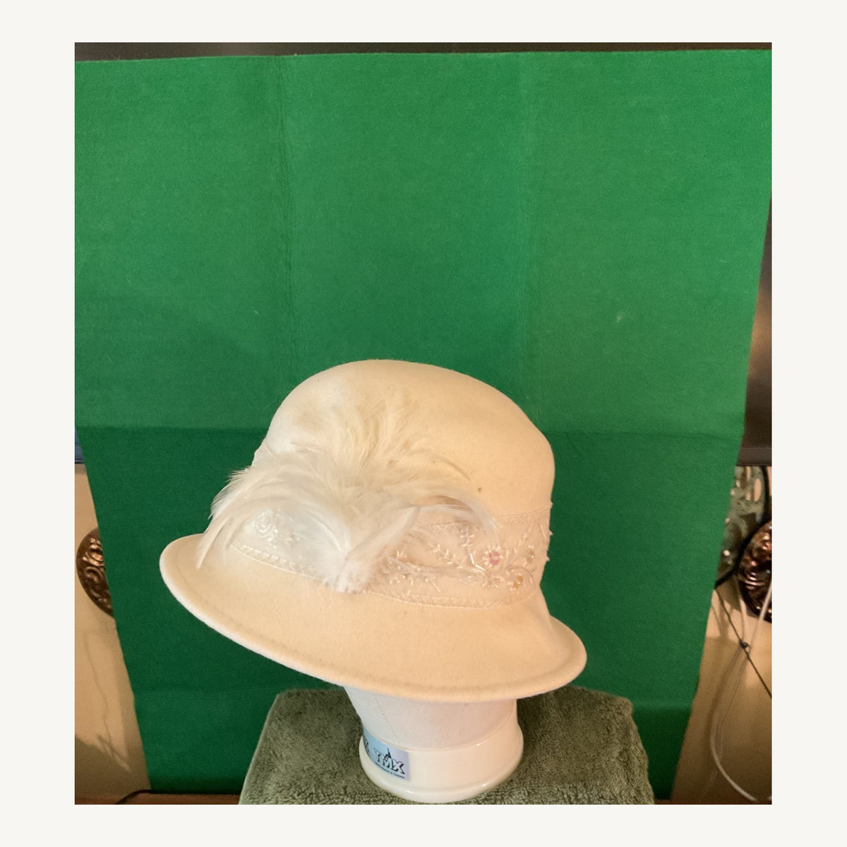 Cream cloche-style occasion hat with feather accent and delicate floral bead detail, pre-owned.
